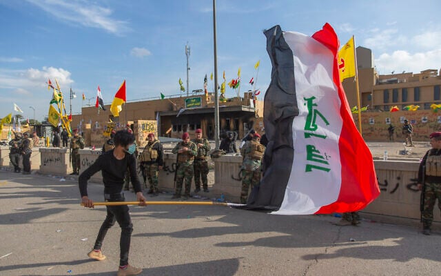 A man waves the Iraqi flag while the Iraqi army soldiers are deployed in front of the US embassy, in Baghdad, Iraq, January 1, 2020. (Nasser Nasser/AP) A man waves the Iraqi flag while the Iraqi army soldiers are deployed in front of the US embassy, in Baghdad, Iraq, January 1, 2020. (Nasser Nasser/AP)