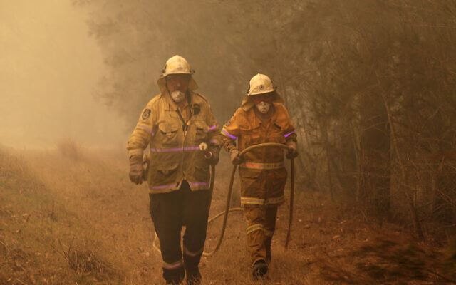 Firefighters drag their water hose after putting out a spot fire near Moruya, Australia, Jan. 4, 2020. (AP Photo/Rick Rycroft)