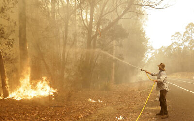 A man uses a water hose to battle a fire near Moruya, Australia, Jan. 4, 2020. (AP Photo/Rick Rycroft)
