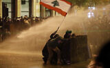 Anti-government protesters wave a Lebanese flag and hide behind a wood barrier from a water cannon as they clash with the riot police during a protest against the new government, near the parliament square, in Beirut, Lebanon, Wednesday, Jan. 22, 2020. (AP/Hussein Malla)