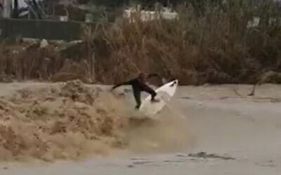 An Israeli man surfing during torrential storms that flooded large parts of the country. (Screenshot)