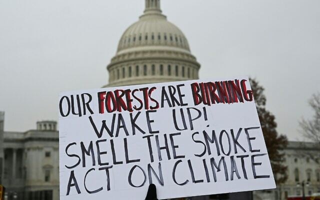 A demonstrator holds a poster in front of the US Capitol during a climate protest in Washington, December 27, 2019. (Eva Hambach/AFP via Getty Images/JTA) A demonstrator holds a poster in front of the US Capitol during a climate protest in Washington, December 27, 2019. (Eva Hambach/AFP via Getty Images/JTA)