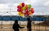 Masked Palestinians prepare to release an incendiary device near Gaza's Bureij refugee camp, along the Israel-Gaza border fence, on February 10, 2020 (MAHMUD HAMS / AFP)