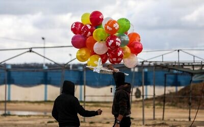 Masked Palestinians prepare to release an incendiary device near Gaza's Bureij refugee camp, along the Israel-Gaza border fence, on February 10, 2020 (MAHMUD HAMS / AFP)