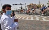 A man wearing a surgical masks looks on as the pack rides by during stage five the UAE Cycling Tour from al-Maroom to Jebel Hafeet, in Dubai on February 27, 2020. (Giuseppe CACACE / AFP)