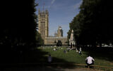 People sit in the sun in Victoria Tower Gardens backdropped by the Houses of Parliament in London, August 28, 2019. (Matt Dunham/AP)