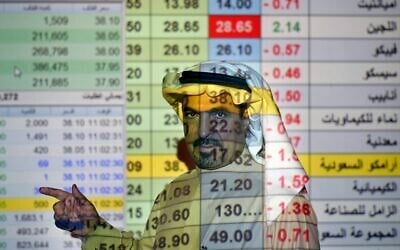A trader talks to others in front of a screen displaying Saudi stock market values at the Arab National Bank in Riyadh, Saudi Arabia,  December 12, 2019. (Amr Nabil/AP)