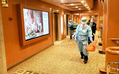 In this February 4, 2020, photo taken by a passenger, medical workers in protective suits walk on the cruise ship Diamond Princess anchored off Yokohama, south of Tokyo (@daxa_tw via AP)