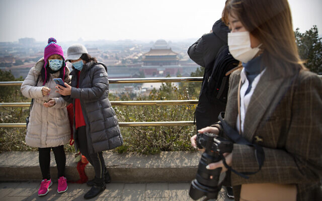 Visitors wearing face masks take photos at a park overlooking the Forbidden City in Beijing, Feb. 28, 2020 (AP Photo/Mark Schiefelbein)