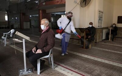An elderly man wearing a protective masks reads from the Quran while seated in a mosque being sterilized by Palestinian Authority health workers in the West Bank city of Ramallah to prevent the spread of the coronavirus, March 7, 2020. (Abbas Momani/AFP)