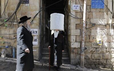 An ultra-Orthodox Jewish boy dressed in a costume as an elderly ultra-Orthodox Jew walks by an elderly ultra-Orthodox Jew (who is not in costume), two days ahead of the official holiday of Purim, in the Mea Shearim neighborhood in Jerusalem, on March 8, 2020. (MENAHEM KAHANA / AFP)