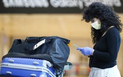 A traveler wearing a protective mask checks her phone at the arrivals hall of Ben Gurion International Airport near Tel Aviv on March 10, 2020. (Jack Guez/AFP)