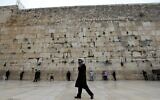 An ultra-Orthodox Jewish man walks past people praying at the nearly deserted Western Wall in Jerusalem's Old City on March 12, 2020. (Emmanuel Dunand/AFP)