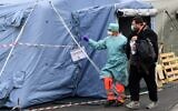 A hospital employee wearing a protection mask and gear, escorts a patient towards the radiology unit at a temporary emergency structure set up outside the accident and emergency department, where any new arrivals presenting suspect new coronavirus symptoms are being tested, at the Brescia hospital, Lombardy, on March 13, 2020. (Miguel Medina/AFP)