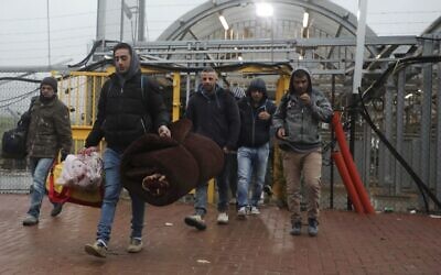 FILE - Palestinian laborers enter Israel to work through a checkpoint between the West Bank city of Hebron and Beersheva while carrying blankets and mattresses on March 18, 2020, as for the first time they have to stay for one to two months inside Israel amid the  coronavirus pandemic. (HAZEM BADER / AFP)