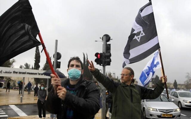 Protesters wave a black flag, an Israeli flag and an Israeli flag with the colors inverted, outside the Knesset in Jerusalem on March 19, 2020. The protest was against the recent decision by the Knesset speaker to shut it down for several days, and against what they described as "damage to Israel's democracy". (MENAHEM KAHANA / AFP) Protesters wave a black flag, an Israeli flag and an Israeli flag with the colors inverted, outside the Knesset in Jerusalem on March 19, 2020. The protest was against the recent decision by the Knesset speaker to shut it down for several days, and against what they described as "damage to Israel's democracy". (MENAHEM KAHANA / AFP)