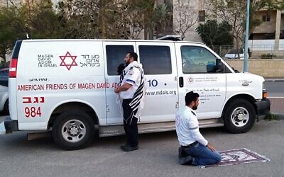 This handout photo provided by the Magen David Adom (MDA) national emergency service on March 24, 2020, in Beersheba shows two paramedics praying outside an ambulance of the American Friends of Magen David Adom (AFMDA): a Jew from Beersheba facing Jerusalem, and an Arab from Rahat facing Mecca (MAGEN DAVID ADOM)