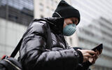 A pedestrian uses her phone while wearing a face mask in Herald Square, Thursday, March 12, 2020, in New York. (AP Photo/John Minchillo)