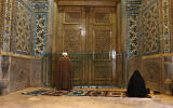 A cleric and a woman pray behind a closed door of the Fatima Masumeh shrine in the city of Qom, Iran, March 16, 2020. (AP Photo)