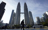 A girl wearing a face mask crossing a road in front of Twin Towers in Kuala Lumpur, Malaysia, March 18, 2020. (AP Photo/Vincent Thian)