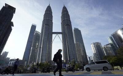 A girl wearing a face mask crossing a road in front of Twin Towers in Kuala Lumpur, Malaysia, March 18, 2020. (AP Photo/Vincent Thian)
