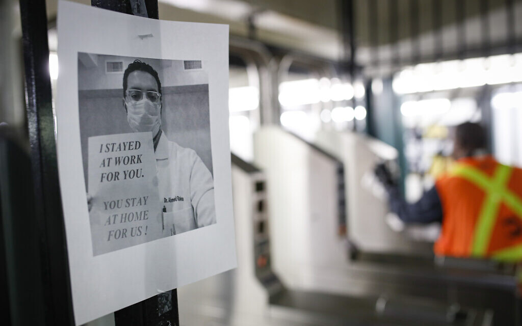 A flier urging customers to remain home hangs at a turnstile as an MTA employee sanitizes surfaces at a subway station with bleach solutions due to COVID-19 concerns, March 20, 2020, in New York. (AP Photo/John Minchillo)