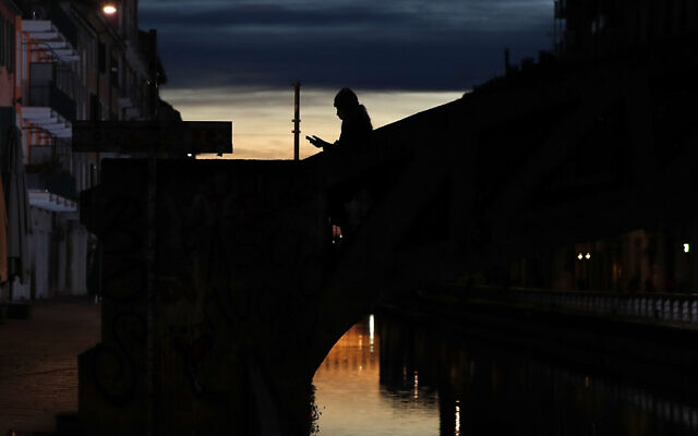 In this March 10, 2020 file photo, a woman wearing a face mask checks her phone as she walks at the Naviglio Grande canal in Milan, Italy. Across Europe, governments are increasingly using surveillance to try to curtail the lethal spread of the new coronavirus, tracking people’s movements with aggregated cell phone location data and introducing apps to keep the infected quarantined. (AP Photo/Antonio Calanni) In this March 10, 2020 file photo, a woman wearing a face mask checks her phone as she walks at the Naviglio Grande canal in Milan, Italy. Across Europe, governments are increasingly using surveillance to try to curtail the lethal spread of the new coronavirus, tracking people’s movements with aggregated cell phone location data and introducing apps to keep the infected quarantined. (AP Photo/Antonio Calanni)