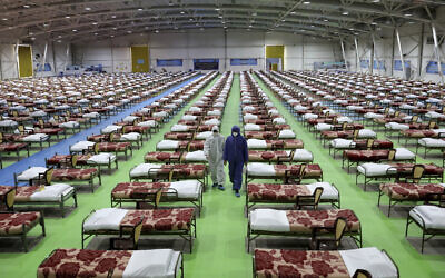 People in protective clothing walk past rows of beds at a temporary 2,000-bed hospital for coronavirus patients set up by the Iranian army at the international exhibition center in northern Tehran, Iran, March 26, 2020. (AP Photo/Ebrahim Noroozi)