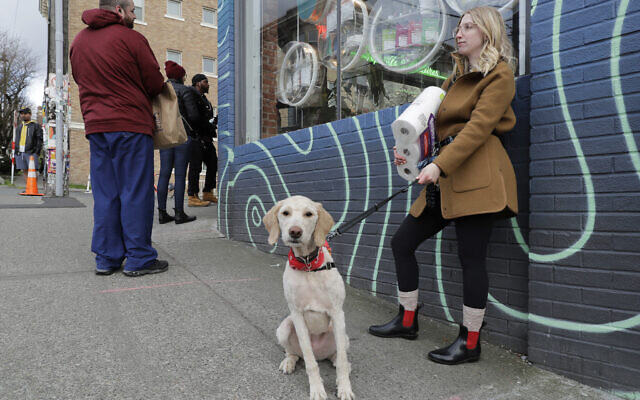 In this photo taken March 24, 2020, Mia Grace, right, holds a package of toilet paper as she and her dog Breezy observe social distancing chalk marks on the sidewalk while waiting to get in to The Reef Capitol Hill, a marijuana store in Seattle, which was limiting the number of people in the store at one time to help slow the spread of the new coronavirus. (AP/Ted S. Warren) In this photo taken March 24, 2020, Mia Grace, right, holds a package of toilet paper as she and her dog Breezy observe social distancing chalk marks on the sidewalk while waiting to get in to The Reef Capitol Hill, a marijuana store in Seattle, which was limiting the number of people in the store at one time to help slow the spread of the new coronavirus. (AP/Ted S. Warren)