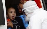 An ultra-Orthodox Jewish boy receives a COVID-19 test by a medical personnel wearing protective gear as part of the government's measures to stop the spread of the coronavirus in the orthodox city of Bnei Brak, a Tel Aviv suburb, March 31, 2020. (AP/Ariel Schalit)