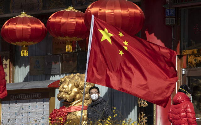 A masked man looks out near a national flag outside a traditional medicine hospital in Beijing on Tuesday, March 3, 2020 (AP Photo/Ng Han Guan) A masked man looks out near a national flag outside a traditional medicine hospital in Beijing on Tuesday, March 3, 2020 (AP Photo/Ng Han Guan)