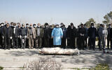 Mourners wearing face masks and gloves pray over the body of former politburo official in the Revolutionary Guard Farzad Tazari, who died Monday after being infected with the new coronavirus, at the Behesht-e-Zahra cemetery just outside Tehran, Iran, March 10, 2020 (Mahmood Hosseini/Tasnim News Agency via AP)