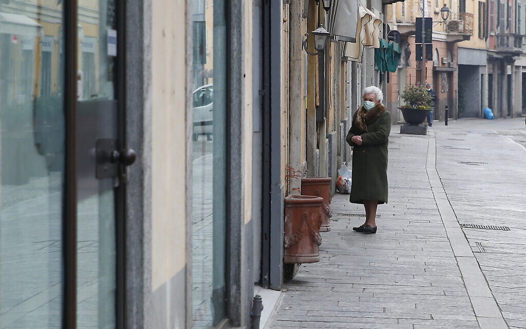 In this photo taken March 12, 2020, an elderly woman wearing a mask waits to enter a deli meat and cold cuts shop in Codogno, Italy. The northern Italian town that recorded Italy’s first coronavirus infection has offered a virtuous example to fellow Italians, now facing an unprecedented nationwide lockdown. (AP Photo/Antonio Calanni)