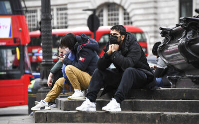 People wear face masks as they sit on the Shaftesbury Memorial Fountain in Piccadilly Circus, in London, March 13, 2020 (AP Photo/Alberto Pezzali)