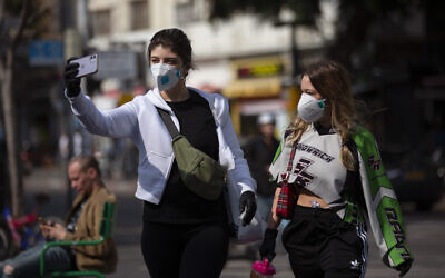 Two women take a selfie as they wear face masks in Tel Aviv, Israel, Sunday, March 15, 2020. (AP/Oded Balilty)
