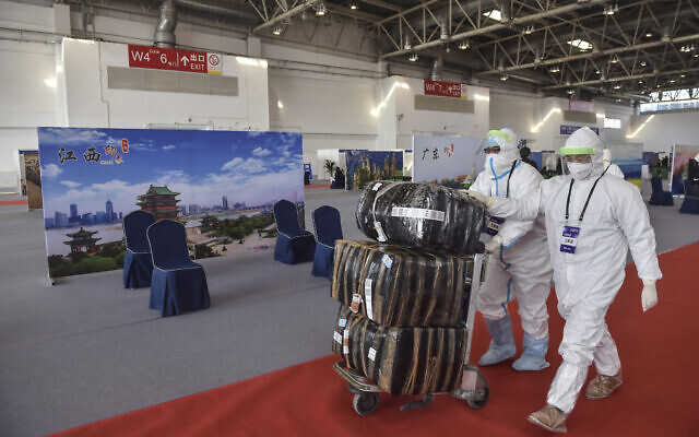 Illustrative: In this March 17, 2020 photo released by China's Xinhua News Agency, workers in protective suits push a cart with passengers' luggage at the New China International Exhibition Center, which has been converted into a facility to screen international flight passengers arriving in Beijing. (Peng Ziyang/Xinhua via AP) Illustrative: In this March 17, 2020 photo released by China's Xinhua News Agency, workers in protective suits push a cart with passengers' luggage at the New China International Exhibition Center, which has been converted into a facility to screen international flight passengers arriving in Beijing. (Peng Ziyang/Xinhua via AP)