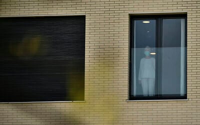 A woman wearing protection mask looks on through the window, at San Martin nursing home, where several elderly people were infected by coronavirus in Vitoria, northern Spain, Thursday, March 19, 2020. Spain will mobilize 200 billion euros or the equivalent to one fifth of the country's annual output in loans, credit guarantees and subsidies for workers and vulnerable citizens, Prime Minister Pedro Sanchez announced Tuesday. For most people, the new coronavirus causes only mild or moderate symptoms. For some, it can cause more severe illness, especially in older adults and people with existing health problems. (AP Photo/Alvaro Barrientos)