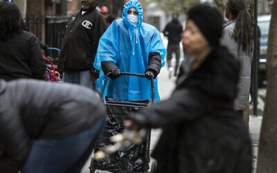 A woman dressed in a poncho, face mask and protective eyewear pushes her grocery cart in the Bedford-Stuyvesant neighborhood of Brooklyn, New York, on Friday, March 20, 2020. New York Gov. Andrew Cuomo is ordering all workers in non-essential businesses to stay home and banning gatherings statewide. Nonessential gatherings of individuals of any size or for any reason are canceled or postponed. (AP Photo/Wong Maye-E)
