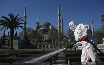 A municipality worker wearing a face mask and protective suits disinfects chairs outside the the historical Sultan Ahmed Mosque, also known as Blue Mosque, amid the coronavirus outbreak, in Istanbul, March 21, 2020 (AP Photo/Emrah Gurel)