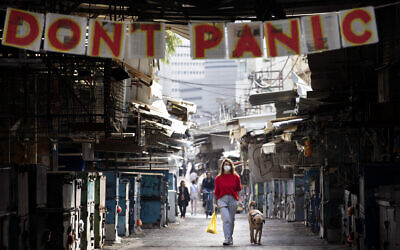A woman walks her dog under a "don't panic" sign hanging on the entrance of the shuttered Carmel Market in Tel Aviv, March 23, 2020. (AP/Oded Balilty)