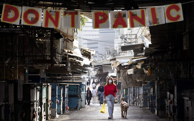 A woman walks her dog under a "don't panic" sign hanging on the entrance of the shuttered Carmel Market in Tel Aviv, March 23, 2020. (AP/Oded Balilty) A woman walks her dog under a "don't panic" sign hanging on the entrance of the shuttered Carmel Market in Tel Aviv, March 23, 2020. (AP/Oded Balilty)