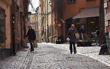 People walk down a quiet cobbled street in Stockholm, March 25, 2020. (AP Photo/David Keyton)