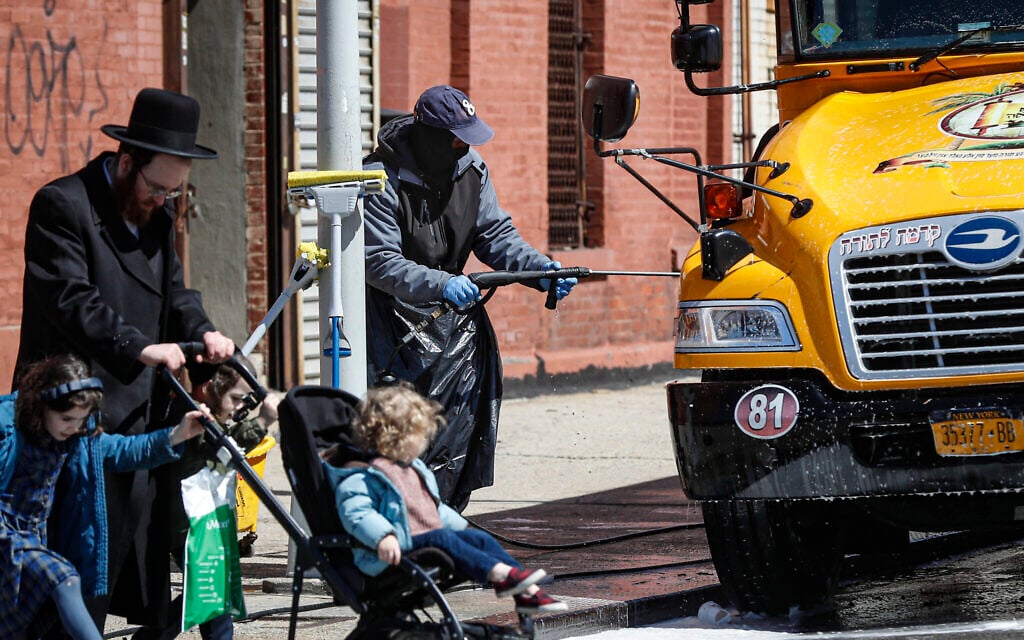 A worker covering in personal protective equipment power washes a school bus that serves an Ultra-Orthodox Jewish community in the Brooklyn borough of New York, March 27, 2020. (AP Photo/John Minchillo)