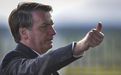 Brazil's President Jair Bolsonaro greets supporters and journalists as he arrives to give a news conference on the new coronavirus at Planalto presidential palace in Brasilia, Brazil, March 27, 2020. (AP Photo/Andre Borges)