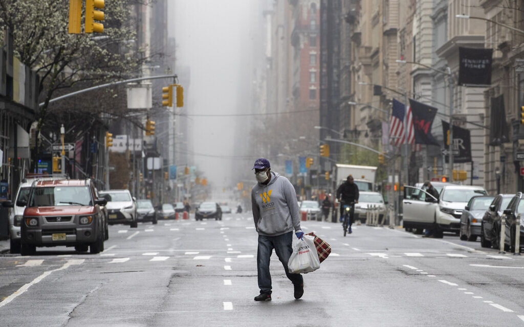 A man wearing a facial mask walks across the middle of 5th Avenue in Midtown Manhattan of New York, March 29, 2020. (AP Photo/Mary Altaffer)