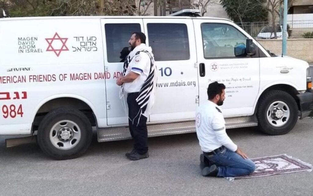 This handout photo provided by the Magen David Adom (MDA) national emergency service on March 24, 2020, in Beersheba shows two paramedics praying outside an ambulance of the American Friends of Magen David Adom (AFMDA): a Jew from Beersheba facing Jerusalem, and an Arab from Rahat facing Mecca. (Magen David Adom) This handout photo provided by the Magen David Adom (MDA) national emergency service on March 24, 2020, in Beersheba shows two paramedics praying outside an ambulance of the American Friends of Magen David Adom (AFMDA): a Jew from Beersheba facing Jerusalem, and an Arab from Rahat facing Mecca. (Magen David Adom)