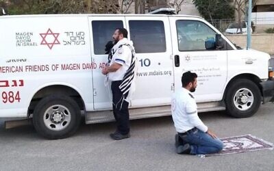 This handout photo provided by the Magen David Adom (MDA) national emergency service on March 24, 2020, in Beersheba shows two paramedics praying outside an ambulance of the American Friends of Magen David Adom (AFMDA): a Jew from Beersheba facing Jerusalem, and an Arab from Rahat facing Mecca. (Magen David Adom)