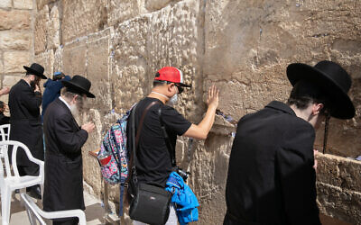 A tourist wearing a face mask for fear of the coronavirus, prays at the Western Wall in the Old City of Jerusalem on February 27, 2020 (Olivier Fitoussi/Flash90)