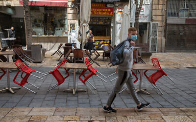 Man wearing a mask walks past closed a cafe in Jerusalem on March 15, 2020 (Nati Shohat/Flash90)