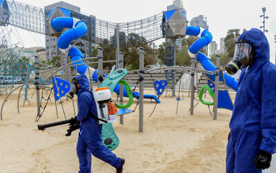 Workers wearing protective clothes disinfect a public playground in the coastal city of Bat Yam, on March 18, 2020 (Flash90)